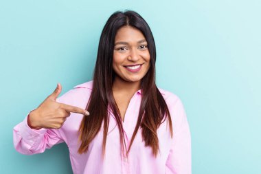 Genç Venezüellalı bir kadın mavi arka planda izole edilmiş. Elle bir gömlek fotokopi alanını işaret ediyor. Gururlu ve kendinden emin.