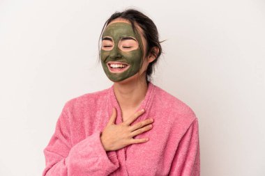 Young caucasian woman wearing a facial mask isolated on white background laughs out loudly keeping hand on chest.