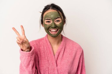 Young caucasian woman wearing a facial mask isolated on white background joyful and carefree showing a peace symbol with fingers.