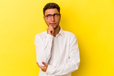 Sarı arka planda izole edilmiş, şüpheli ve şüpheci bir ifadeyle yan bakan beyaz dövmeli genç bir adam..