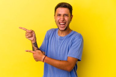 Sarı arka planda izole edilmiş beyaz dövmeli genç bir adam işaret parmağıyla işaret ederek heyecanlanıyor..