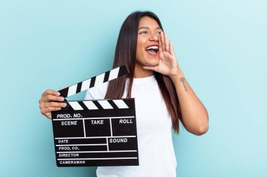 Genç Venezuelalı bir kadın mavi arka planda izole edilmiş bir klempon tutuyor bağırıyor ve avuç içini açık tutuyordu..