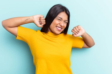 Genç Venezuelalı kadın, mavi arka planda izole edilmiş, kollarını açmış, rahat bir konumda..