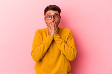 Sarı arka planda izole edilmiş, ağzı ellerle kaplanmış, yeni bir şey keşfetmek için sabırsızlanan beyaz dövmeli genç bir adam..