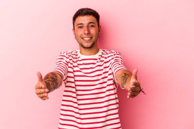 Sarı arka planda dövmeleri olan beyaz bir genç hoş bir yüz ifadesi sergiliyor..