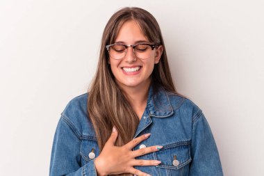 Beyaz arka planda izole genç beyaz kadın mutlu bir şekilde gülüyor ve ellerini karnının üstünde tutarak eğleniyor..