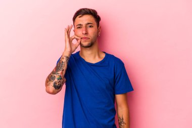 Sarı arka planda dövmeleri olan genç beyaz bir adam. Parmakları dudaklarında bir sır saklıyor..