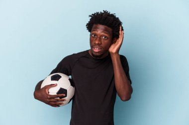 Amerikan futbolu oynayan genç Afrikalı bir adam mavi arka planda izole edilmiş bir şekilde bir dedikoduyu dinlemeye çalışıyor..