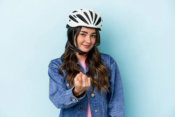 Young caucasian woman rinding a bike isolated on blue background pointing with finger at you as if inviting come closer.