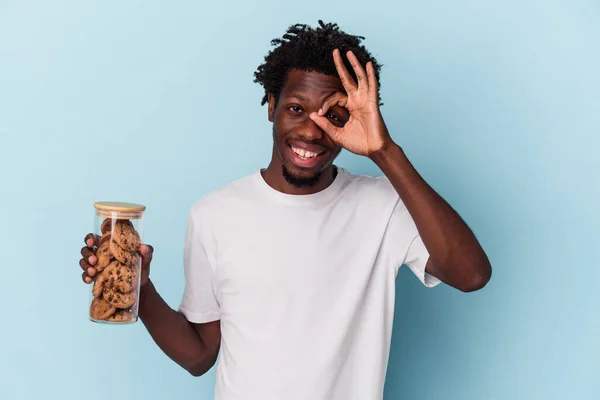 若いですアフリカ系アメリカ人男性保持チョコレートチップクッキー隔離上の青背景励起保つ上でOkジェスチャー上の目 — ストック写真