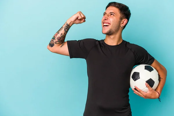 Młody Człowiek Gra Piłkę Nożną Trzymając Piłkę Niebieskim Tle Podnosząc — Zdjęcie stockowe
