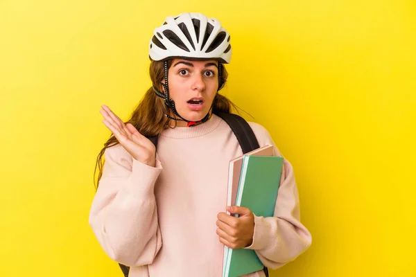 若いですCaucasian学生女性身に着けていますAバイクヘルメット隔離上の黄色の背景驚きとショック — ストック写真