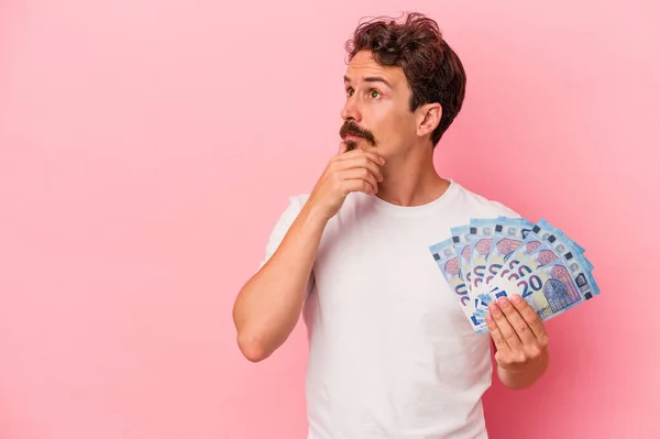 Young Caucasian Man Holding Banknotes Isolated Pink Background Looking Sideways — Stock Photo, Image