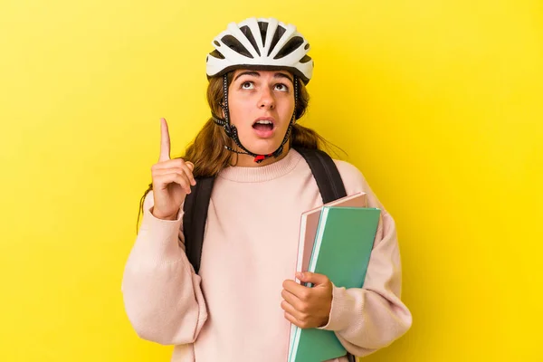 若いですCaucasian学生女性身に着けていますAバイクヘルメット隔離上の黄色の背景ポインティングアップサイドでオープン口 — ストック写真