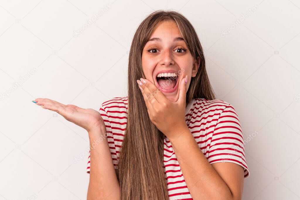 Young caucasian woman isolated on white background holds copy space on a palm, keep hand over cheek. Amazed and delighted.