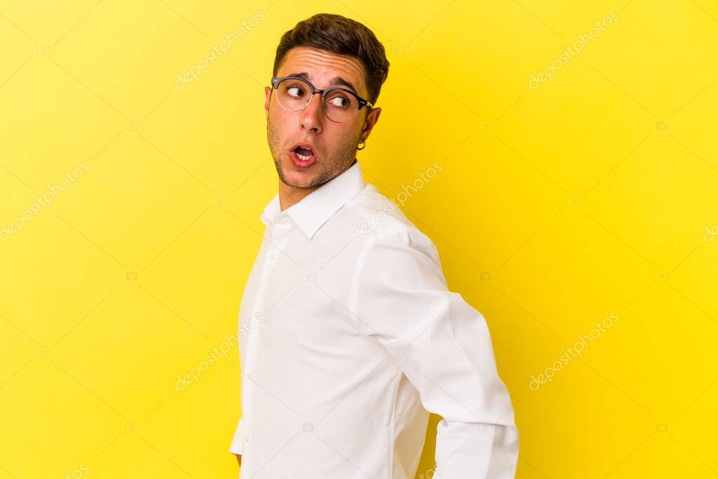 Young caucasian man with tattoos isolated on yellow background  looks aside smiling, cheerful and pleasant.
