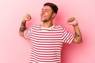 Sarı arka planda izole edilmiş, kollarını esneten, rahat bir pozisyonda dövmeleri olan genç beyaz bir adam..