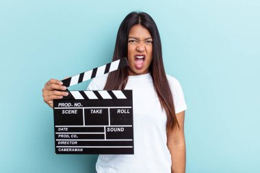 Genç Venezuelalı bir kadın mavi arka planda izole edilmiş bir alçıpan tutuyor. Çok sinirli ve agresif bağırıyor..