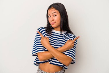 Beyaz arka plan noktalarında izole edilmiş genç Latin kadın iki seçenek arasında seçim yapmaya çalışıyor..