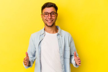 Sarı arka planda dövmeleri olan beyaz bir adam iki eliyle bir şey tutuyor, ürün sunumu..