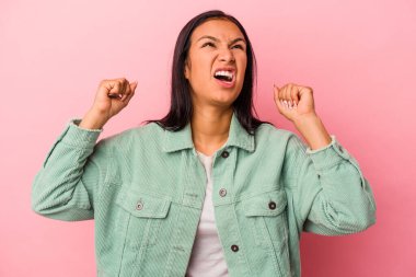 Pembe arka planda izole edilmiş genç Latin kadın zaferden sonra yumruk kaldırıyor, kazanan konsept..