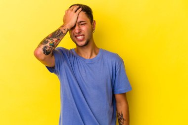 Sarı arka planda izole edilmiş dövmeleri olan genç beyaz bir adam bir şeyi unutuyor. Alnına avuç içi ve kapalı gözlerle tokat atıyor..