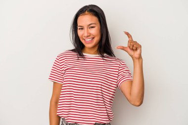 Beyaz arka planda izole edilmiş genç Latin bir kadın işaret parmaklarıyla küçük bir şey tutuyor, gülümsüyor ve kendinden emin..