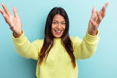 Genç Venezuelalı kadın mavi arka planda izole edilmiş zaferi ya da başarıyı kutluyor, şaşırmış ve şok olmuş..