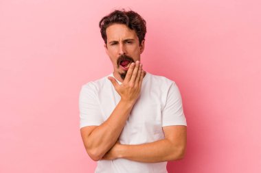 Pembe arka planda izole edilmiş genç beyaz adam esniyor. Ağzı eliyle kapatan yorgun bir hareket sergiliyor..