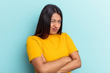 Genç Venezuelalı bir kadın mavi arka planda izole edilmiş hoşnutsuzca kaşlarını çatmış, kollarını kavuşturmuş.