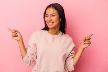 Pembe arka planda izole edilmiş genç Latin bir kadın farklı kopya alanlarını gösteriyor, birini seçiyor, parmaklarıyla gösteriyor.