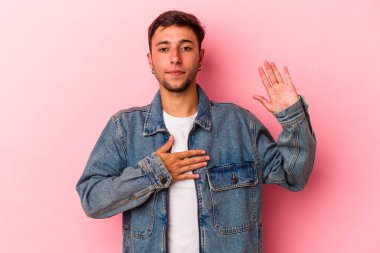 Sarı arka planda izole edilmiş dövmeleri olan beyaz genç bir adam yemin ediyor, elini göğsüne koyuyor..