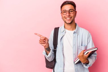 Elinde pembe arka planda izole edilmiş kitaplar tutan beyaz bir genç adam gülümsüyor ve boş alanda bir şeyler gösteriyor..