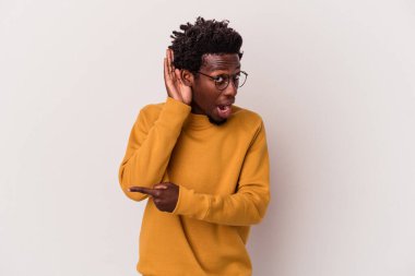 Genç Afrikalı Amerikalı adam beyaz arka planda izole edilmiş bir şekilde bir dedikoduyu dinlemeye çalışıyor..