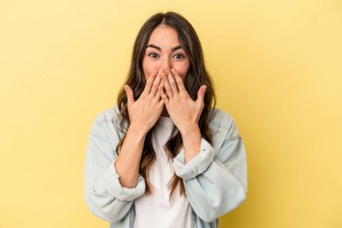 Sarı arka planda izole edilmiş genç beyaz kadın elleriyle ağzını kapatırken şok oldu..