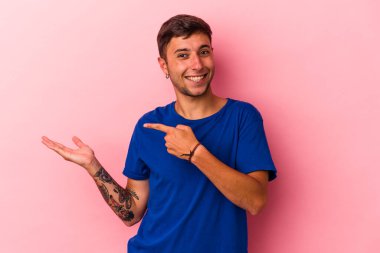 Sarı arka planda izole edilmiş dövmeleri olan genç beyaz bir adam, palmiye ağacında bir kopya alanı tutarken heyecanlanıyor..