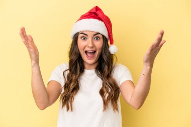 Genç beyaz kadın, sarı arka planda izole edilmiş bir şekilde Noel 'i kutluyor. Hoş bir sürprizle karşılaşıyor, heyecanlı ve el kaldırıyor..