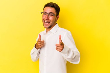 Sarı arka planda izole edilmiş, parmaklarıyla ön tarafı gösteren dövmeleri olan genç beyaz bir adam..