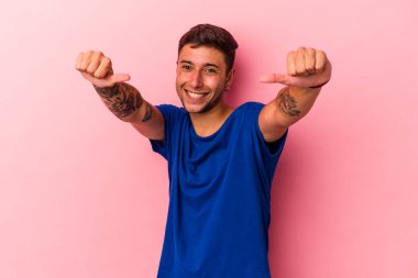 Sarı arka planda izole edilmiş beyaz dövmeli genç bir adam. Baş parmağını kaldırıyor, gülümsüyor ve kendinden emin..