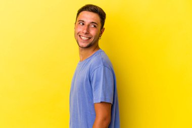 Sarı arka planda izole edilmiş dövmeleri olan beyaz bir genç gülümsüyor ve keyifli görünüyor..