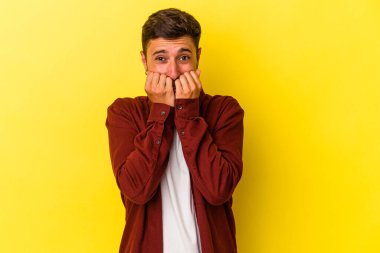 Sarı arka planda izole edilmiş, tırnak yiyen, gergin ve endişeli dövmeleri olan genç beyaz bir adam..