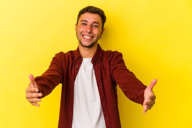 Sarı arka planda dövmeleri olan beyaz bir genç hoş bir yüz ifadesi sergiliyor..