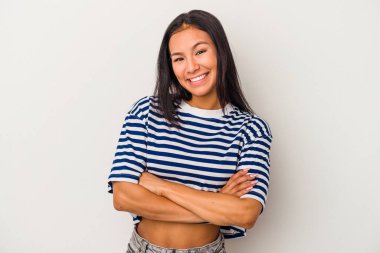 Beyaz arka planda kendini güvende hisseden, kararlılıkla kol kola giren genç Latin bir kadın..