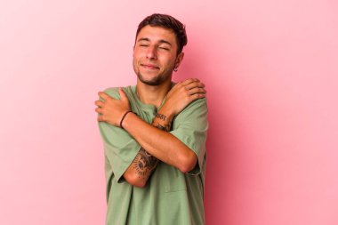 Sarı arka plan kucaklamalarında izole edilmiş dövmeleri olan genç beyaz bir adam. Gülümsüyor ve mutlu..