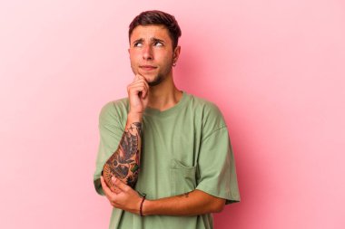 Sarı arka planda izole edilmiş, şüpheli ve şüpheci bir ifadeyle yan bakan beyaz dövmeli genç bir adam..