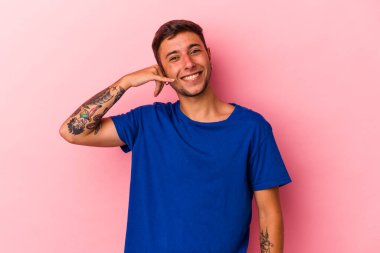 Sarı arka planda izole edilmiş dövmeleri olan genç beyaz bir adam parmakları olan bir cep telefonu hareketi gösteriyor..