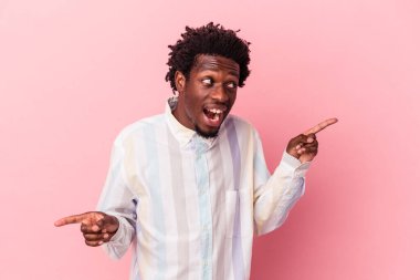 Pembe arka planda izole edilmiş genç Afrikalı Amerikalı adam farklı fotokopi alanlarını gösteriyor, birini seçiyor, parmaklarıyla gösteriyor..