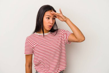 Beyaz arka planda izole edilmiş genç Latin kadın uzaklara bakıyor ve elini alnına koyuyor..