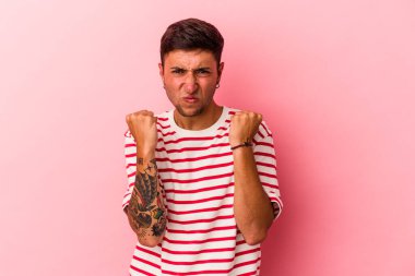 Sarı arka planda izole edilmiş dövmeleri olan genç beyaz bir adam kameraya yumruk gösteriyor, agresif bir yüz ifadesi var..