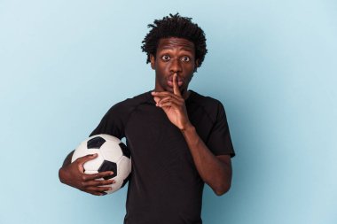 Genç Afro-Amerikan futbol oynayan adam mavi arka planda izole edilmiş bir şekilde bir sır saklıyor ya da sessizlik istiyor..